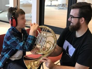 Child with earmuffs trying a horn at a Music Circle event